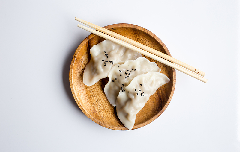two dumplings on a wood plate with chopsticks